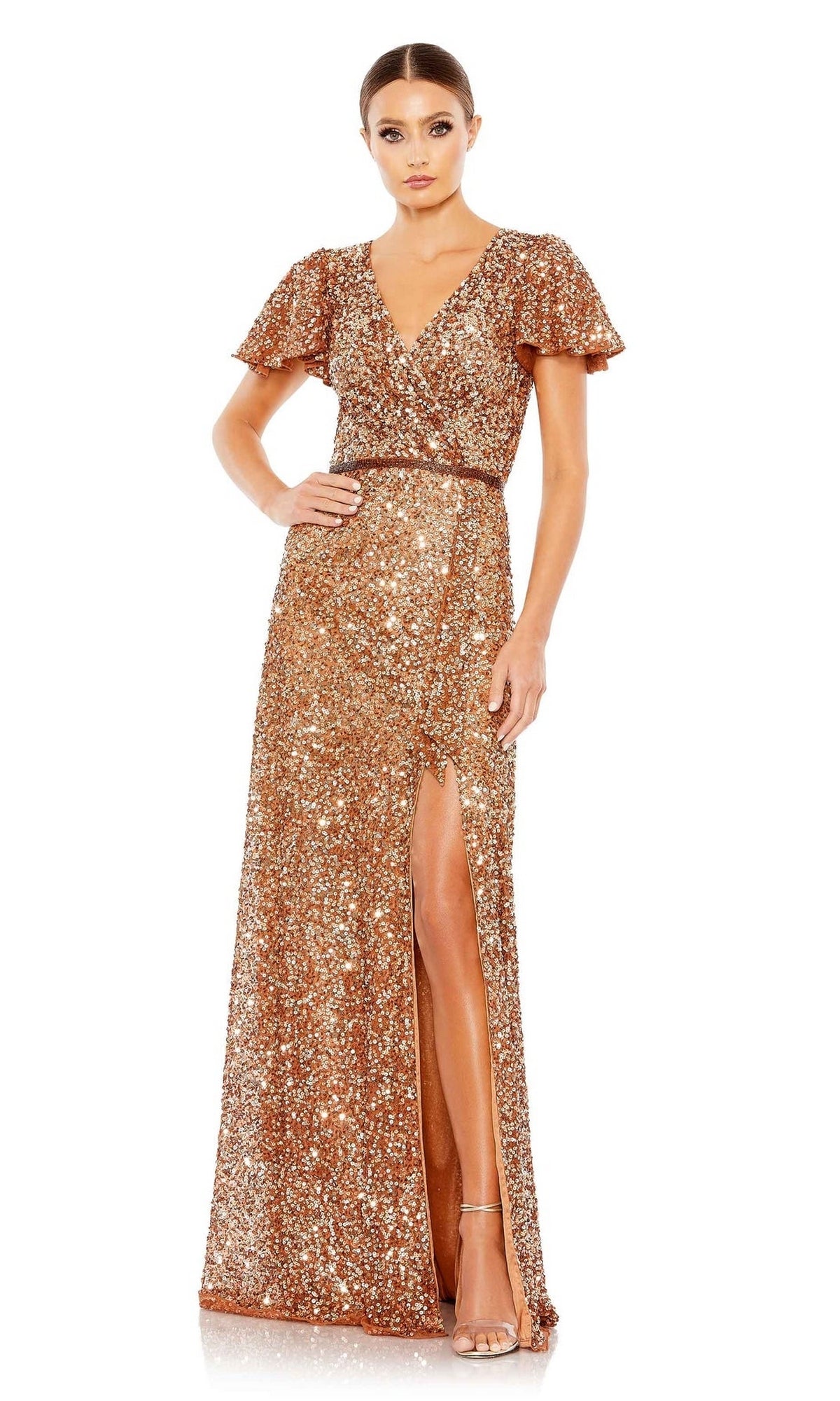 A woman wears the Mac Duggal 5540 Short-Sleeve Sequin Formal Dress—a floor-length gold gown with flutter sleeves, V-neckline, and front slit. She poses with one hand on her hip and strappy heels.